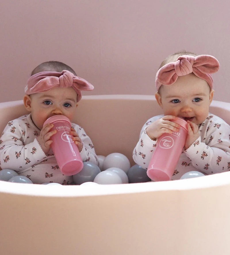 Two babies with pink bows drinking from Twistshake bottles